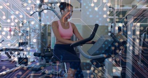 Female athlete pedaling stationary bike with futuristic digital circuitry overlay