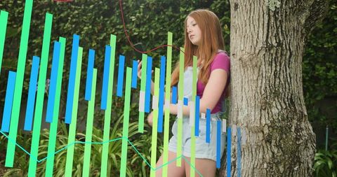 Young woman leaning on tree checking smartphone with colorful analytics overlay in garden