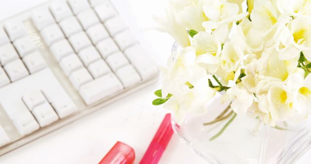 Close up of white flowers in bottle and computer keyboard. Home office, remote working and domestic life, flowers and home decoration.