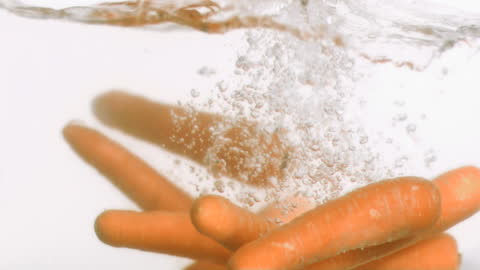 Fresh Carrots Splashing into Water in Slow Motion