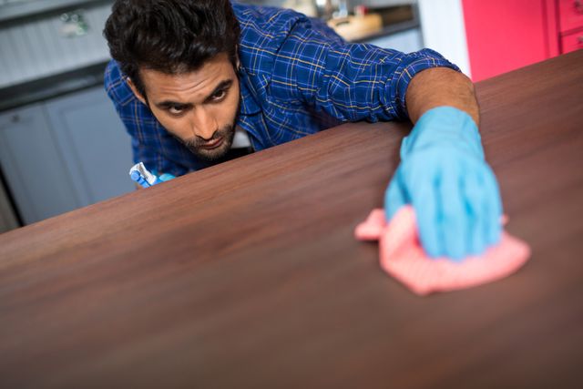 Man cleaning wooden table with napkin at home