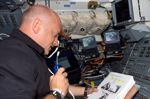 S121-E-05914 (7 July 2006) --- Astronaut Mark E. Kelly, STS-121 pilot, uses a communication system as he refers to a procedures checklist on the aft flight deck of the Space Shuttle Discovery.