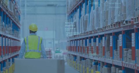 Warehouse worker walking aisle pushing pallet wearing yellow hard hat neon safety vest