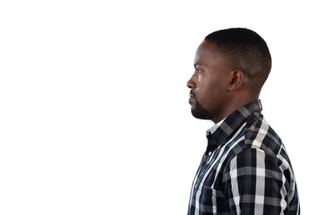 This image shows a thoughtful man standing in profile against a white background. He is wearing a plaid shirt and appears to be in deep contemplation. This image can be used for articles on introspection, personal growth, or mental health. It is also suitable for advertisements or websites focusing on men's fashion, casual wear, or lifestyle content.