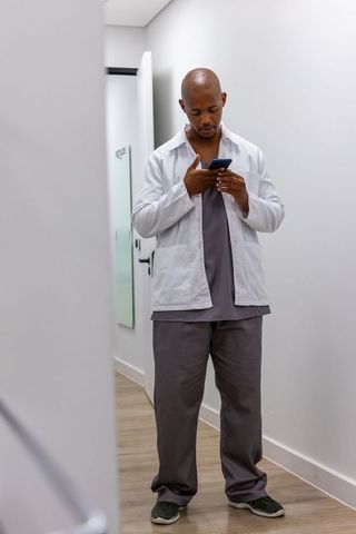 Clinician checking smartphone in clinical corridor wearing lab coat and scrubs