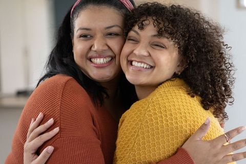 African american friends hugging and smiling in cozy rust and mustard sweaters, close-up