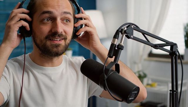 Male podcast host adjusting headphones in home studio with boom microphone and warm light