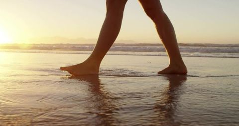 Barefoot Woman Walking Along Tranquil Beach at Sunset