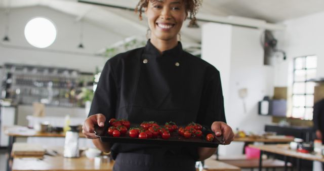 Smiling chef showcasing tray of freshly prepared tomatoes in modern kitchen. Suitable for culinary blogs, restaurant promotions, food preparation websites, or professional chef portfolios.