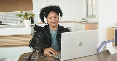 African american man podcasting in minimalist kitchen with laptop headphones microphone