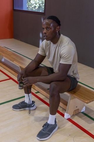 African american athlete resting on bench holding jump rope on indoor court