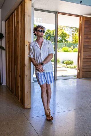 Adult man leaning on wood partition in modern home wearing striped shorts