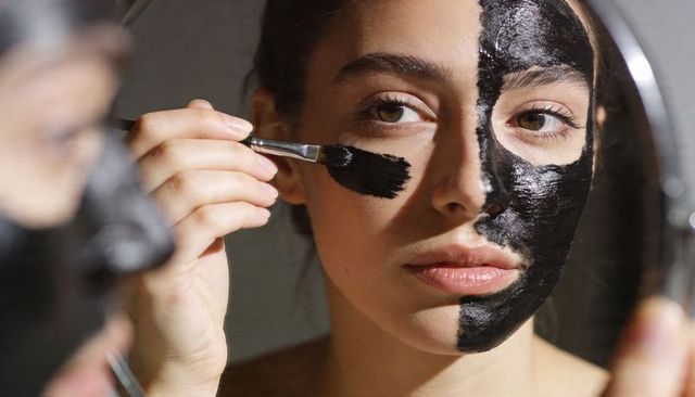 Applying half-face charcoal mask with brush closeup mirror beauty routine skincare