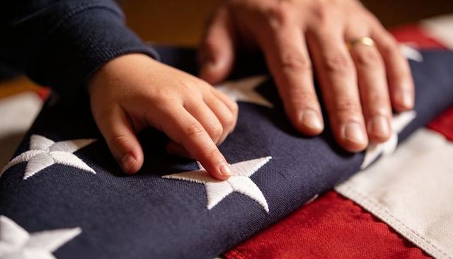 Child touching stitched star on folded american flag with parent hand and wedding ring