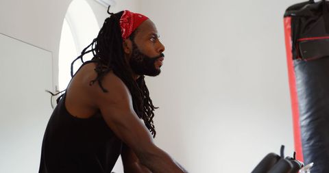 Side view of a dedicated male boxer intensively working out in a modern fitness studio. The athletic individual is punching or engaging with gym equipment, focusing intently on enhancing physical strength and boxing skills. This image is ideal for use in topics related to fitness motivation, boxing training methods, gym promotions, and health improvement stories.