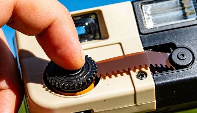 Fingertip advancing film on vintage compact camera macro closeup with sprocket gear