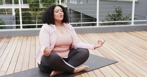 African American woman meditating on rooftop deck in pink activewear for mindfulness