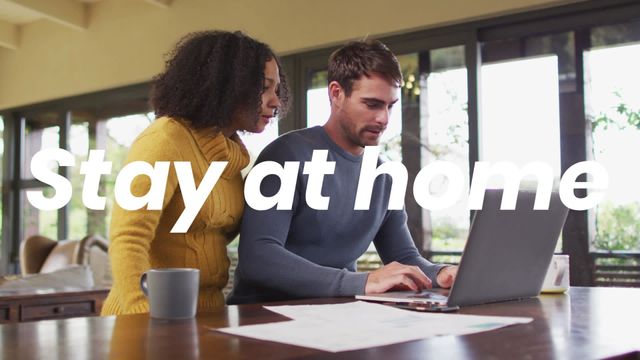 Diverse couple working together on a laptop in a home office setting. Both individuals are focused, with the woman peering over the man's shoulder. A mug sits on the desk beside them, adding to the casual and homely atmosphere. Ideal for promoting remote work, home office setups, teamwork, productivity, and inclusive work environments.