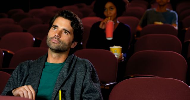 Man sits in a largely empty movie theater, appearing contemplative while watching a film. Perfect for advertisements about cinemas, film festivals, movie promotions, or articles discussing the movie-going experience or solitary pastimes.