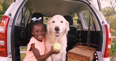 Cheerful Girl Playing with Retriever in Car Trunk on Sunny Afternoon