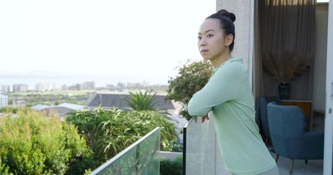 Asian Woman Leaning on Balcony Railing Overlooking Scenic Coastal Skyline