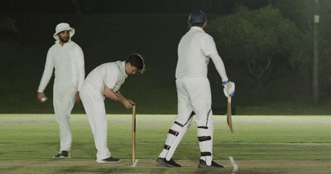 Cricket players adjusting stumps and preparing to bat under floodlights at night