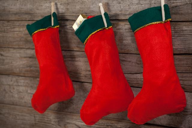 Three red Christmas stockings with green trim hanging on a rustic wooden wall. Ideal for holiday-themed promotions, festive greeting cards, seasonal advertisements, and Christmas decoration inspiration.