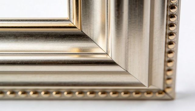 Close-up ornate silver-gold picture frame corner with beaded trim and mitered joint