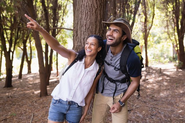 Happy woman pointing to man in forest during hiking