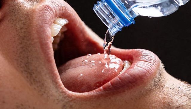 Pouring water into open mouth closeup showing tongue droplets hydration macro texture