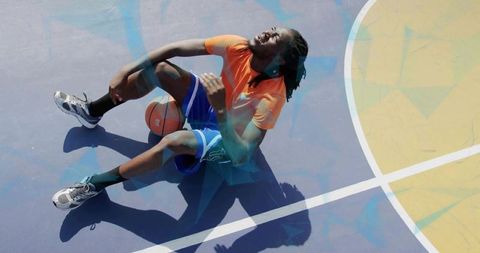 Sunlit outdoor basketball player holding knee after fall on blue hardcourt, sports injury
