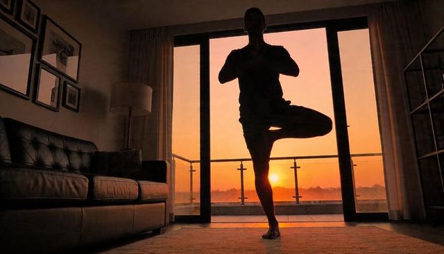 Sunrise living room yoga silhouette practicing tree pose on balcony with warm golden light