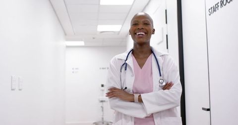 Smiling female doctor standing in clinic corridor wearing lab coat and stethoscope