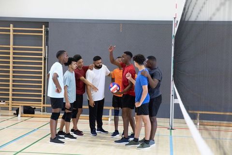 Diverse male volleyball team huddling and strategizing near net on indoor court