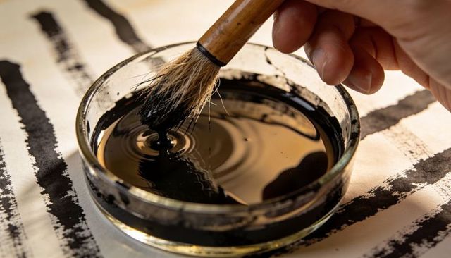 Right hand dipping bamboo brush into sumi ink dish with bold calligraphy brush strokes