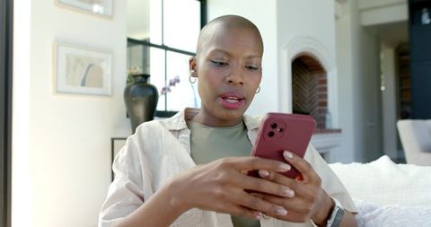 African woman reading aloud on smartphone in bright minimalist living room