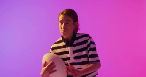 Woman holding rugby ball on pink and purple gradient background wearing striped jersey