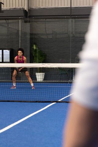 Focused african american woman competing at net on blue indoor paddle court