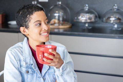African american woman in denim jacket holding red mug and smiling at cozy cafe counter