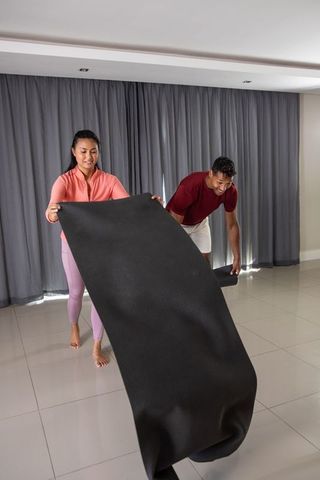 Diverse couple preparing exercise mat at home for fitness routine