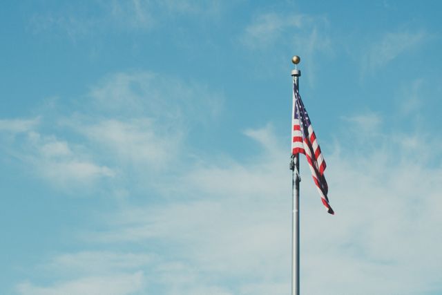 The American flag is waving majestically on a flagpole against a clear, blue sky. The stars and stripes stand out vibrantly, symbolizing patriotism and the United States. This image is perfect for use in political campaigns, national holidays like Independence Day, educational materials, or any project celebrating American pride.