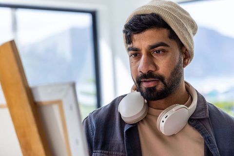 Artist examining canvas in sunlit studio with beanie and headphones