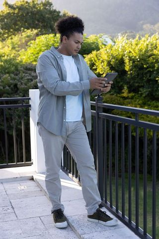African american man tapping tablet on balcony overlooking lush garden during daylight