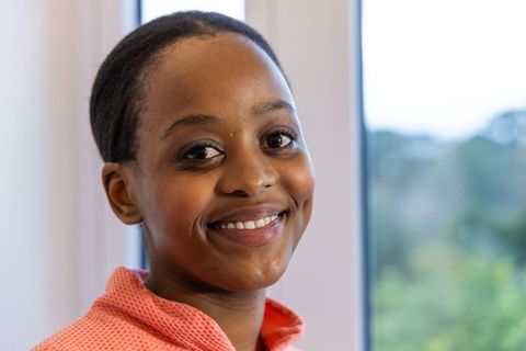 African american teen smiling closeup by window wearing coral pink zip-up top