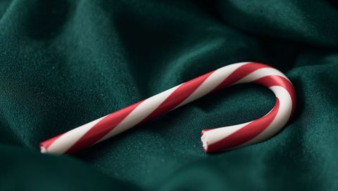 Red-and-white candy cane resting on emerald satin fabric with broken end close-up