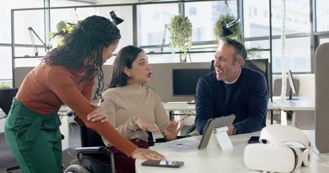 Diverse team collaborating in modern open-plan office with tablet, VR headset, wheelchair