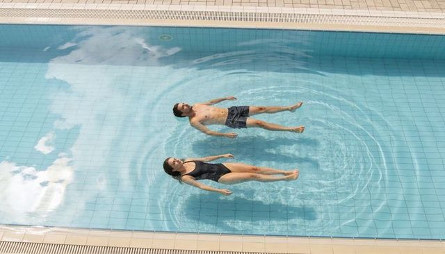 Couple floating on backs in sunlit blue tile pool creating calm ripples