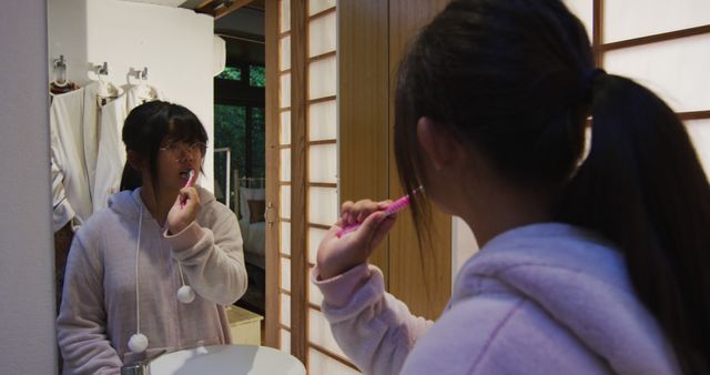 Teenage girl brushing teeth in modern bathroom setting, reflected in mirror. Suitable for themes related to personal hygiene, morning routines, self-care, teenage life, or bathroom product advertisements.
