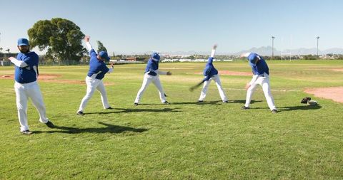 Baseball players in uniform practicing swing on field