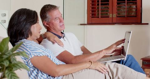 Senior couple relaxing on sofa with laptop in a cozy living room